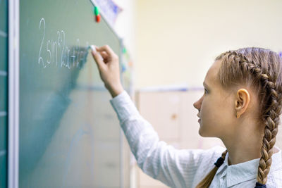Side view of girl writing on chalkboard