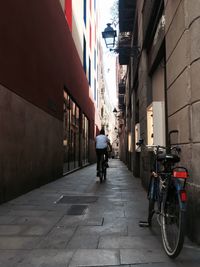 Rear view of man riding bicycle on street amidst buildings in city