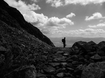 Silhouette man standing on rocks against cloudy sky