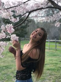 Portrait of young woman standing by cherry blossom