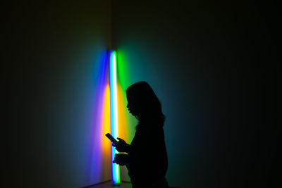 Side view of silhouette man using smart phone against black background