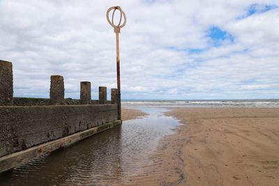 Beach groyne at low tide with circular marking post set against cloudy skies