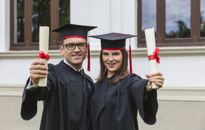 Portrait of smiling man and woman holding certificates against wall