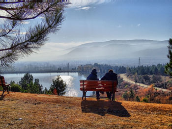 Rear view of friends sitting on bench against lake