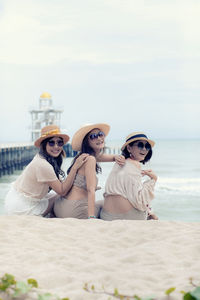 Portrait of smiling women sitting on beach against sea