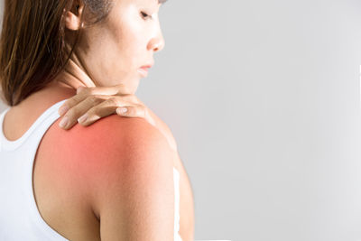 Close-up of woman suffering from shoulder pain against gray background