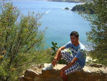 High angle portrait of man sitting on retaining wall against sea