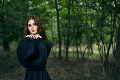 Portrait of young woman standing against trees