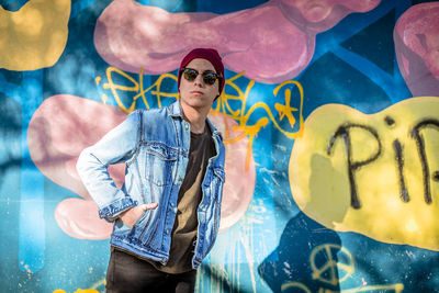 Young woman wearing sunglasses standing against graffiti wall