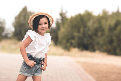 Smiling child girl 4-5 year old wear straw hat, top and denim shorts in park outdoors. summer season