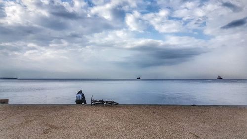 Rear view of man sitting on jetty against lake