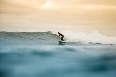 Man surfing in sea against sky during sunset