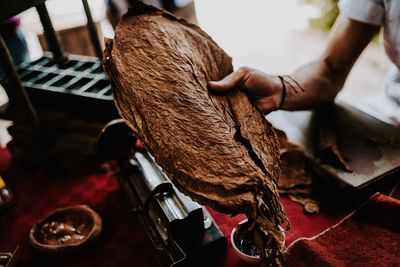 Cropped hand of craftsperson holding dry tobacco leaves at workshop