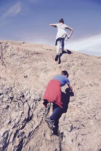 Siblings climbing on rock against sky