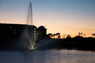 Fountain by river against sky during sunset