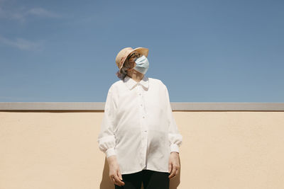 Senior woman with protective face mask in front of blue sky