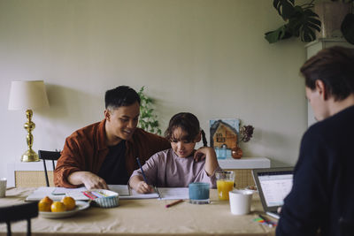 Gay father assisting daughter while doing homework at home