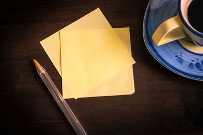 Desk with yellow notes squares sheets of paper, a pen and a cup of black espresso coffee