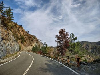 Empty road by trees against sky