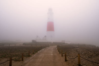 Lighthouse amidst buildings against sky during foggy weather