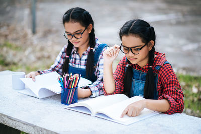 Friends reading book while sitting against trees