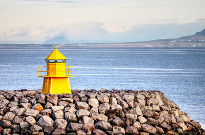 Yellow lighthouse by sea against cloudy sky