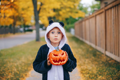 Portrait of cute boy holding pumpkin standing on footpath