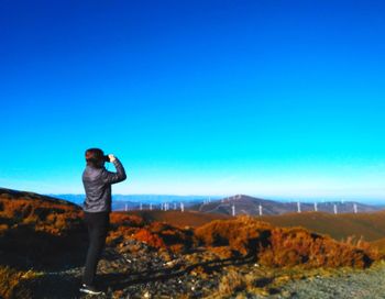 Man photographing on mountain against clear blue sky