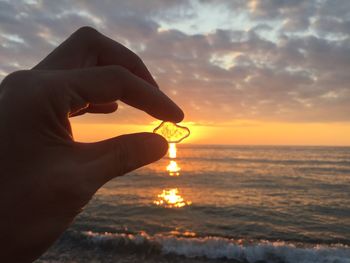 Cropped hand of person holding stone against sky during sunset