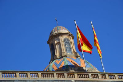 Low angle view of flags on building against blue sky with flags