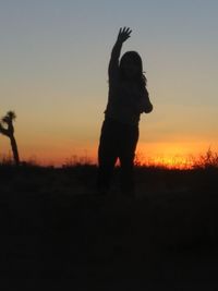 Silhouette woman standing on field against sky during sunset