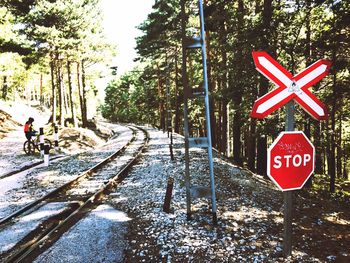 Road sign by railroad tracks against sky