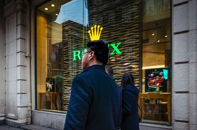 Rear view of man standing against illuminated building at night