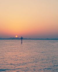 Silhouette person standing in sea against sky during sunset