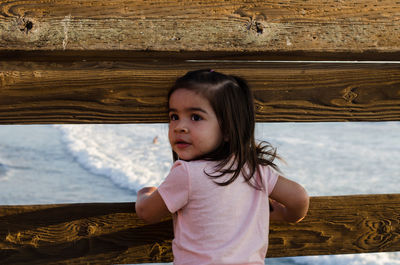 Girl looking away while standing by wooden railing