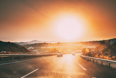 Road leading towards city against sky during sunset