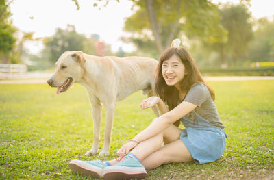 Portrait of young woman sitting on grass with dog