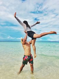 Full length of young woman with arms outstretched standing at beach