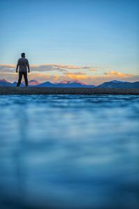 Rear view of man looking at mountains while standing against sky during sunset