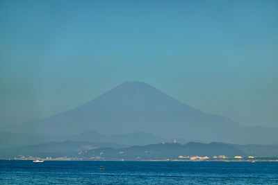 Scenic view of sea and volcano against clear blue sky