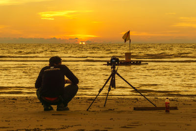 Rear view of man on beach against sky during sunset