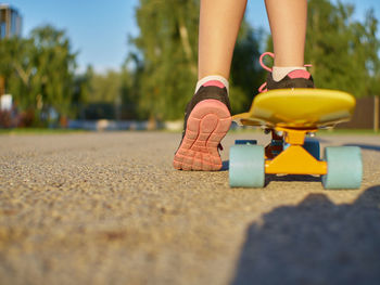 Girl  standing on the asphalt road and yellow penny board with blue wheels on street background.
