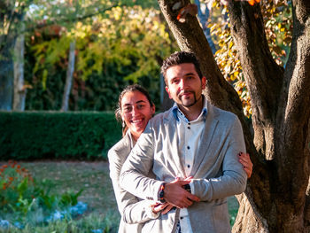 Portrait of smiling couple standing against tree in park