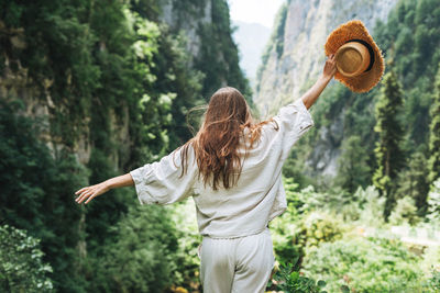 Young woman traveler with long blonde hair in straw hat looks at beautiful view of mountains