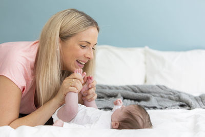 Mother kissing baby girl feet on bed at home