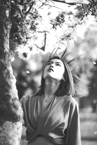 Portrait of young woman standing against tree