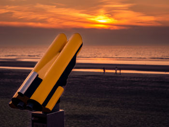 Binoculars overseeing a colorful sunset at the beach with the sun peeking below a cloudlayer
