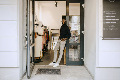Portrait of smiling owner standing at doorway of clothing store