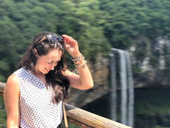 Smiling woman with eyes closed standing against waterfall