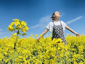 Young woman standing amidst yellow flowering plants on field against sky